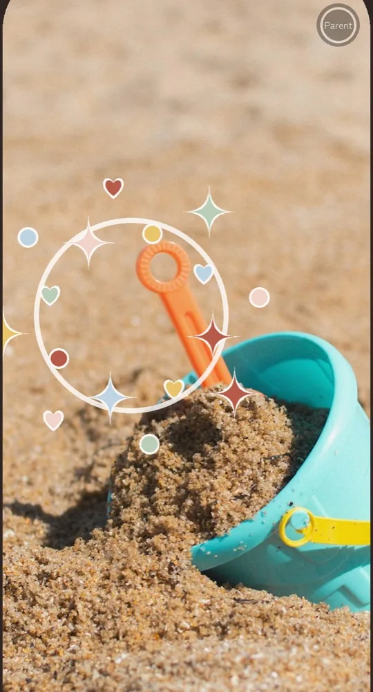 The shooting screen. A sandbox shovel is in frame, and a white ring with stars and hearts bursts from where the screen was touched